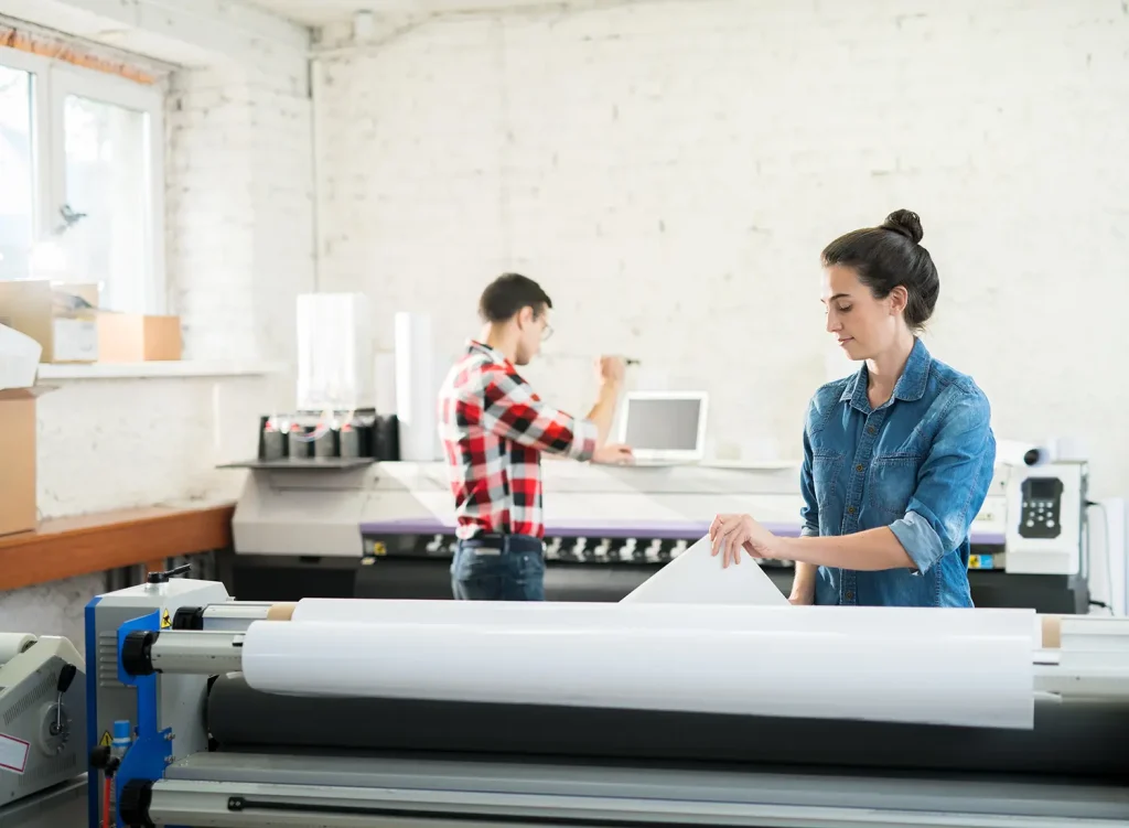 A photograph of two young professionals working with the heat set wrapping in a print shop.