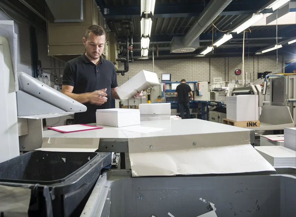 A young caucasian man working in the boxing station of a print shop.